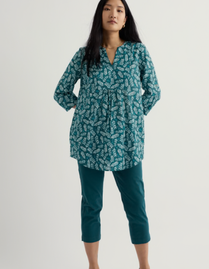 Woman wearing a teal patterned blouse and pants on a white background