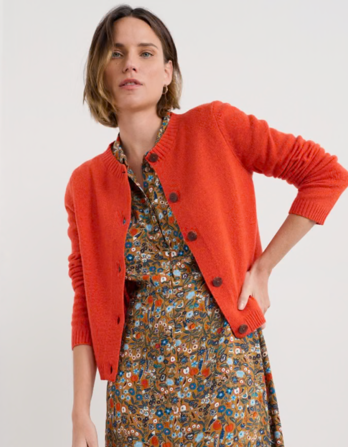 Woman wearing an orange cardigan over a patterned dress on a white background