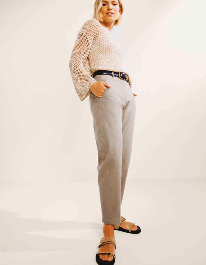 Person wearing a beige sweater and light gray pants on a white background