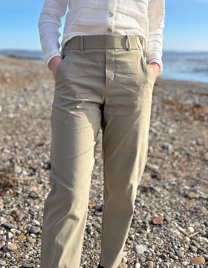 Person wearing beige pants and a white shirt on a pebbly beach with ocean in the background