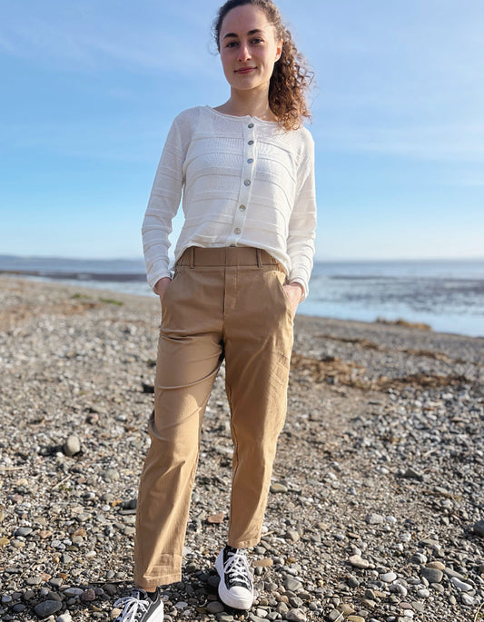 Person standing on a pebbly beach wearing a white shirt and beige pants.