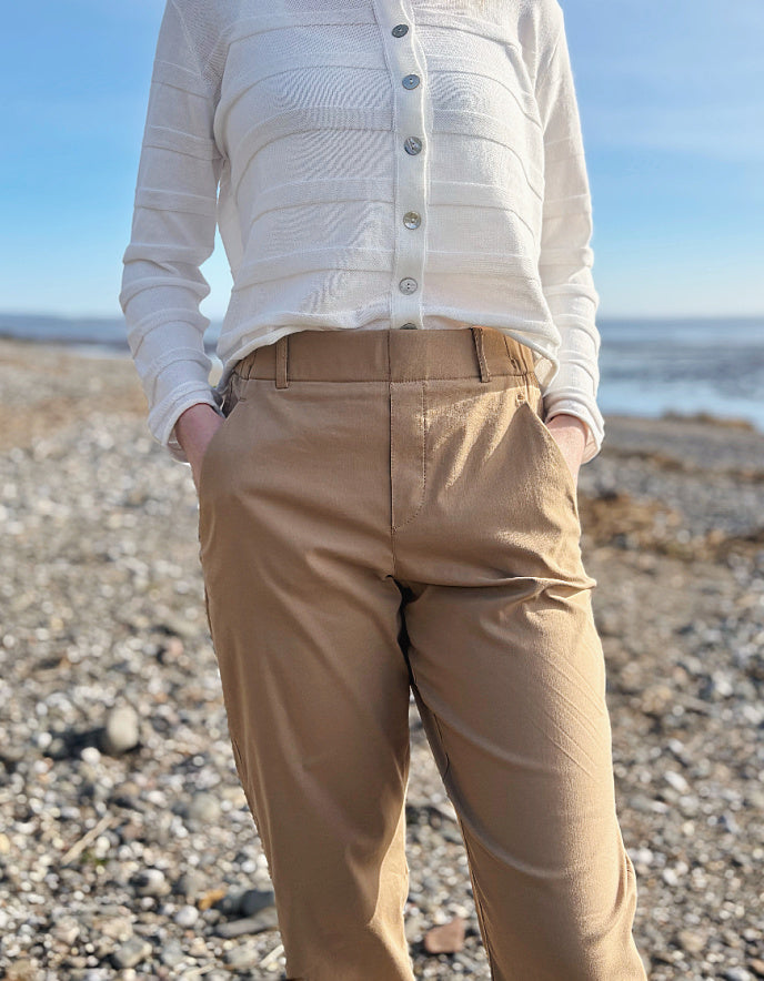 Person wearing a white shirt and beige pants standing on a pebbly beach with ocean in the background