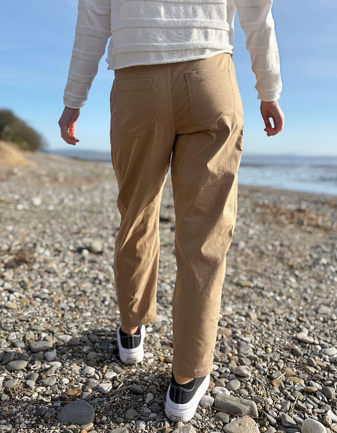 Person wearing beige pants and a white jacket standing on a pebbly beach.