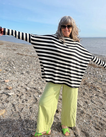 Person wearing a black and white striped poncho and green pants on a beach.