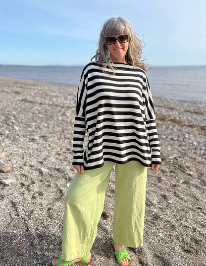 Woman wearing a black and white striped sweater and green pants standing on a beach.