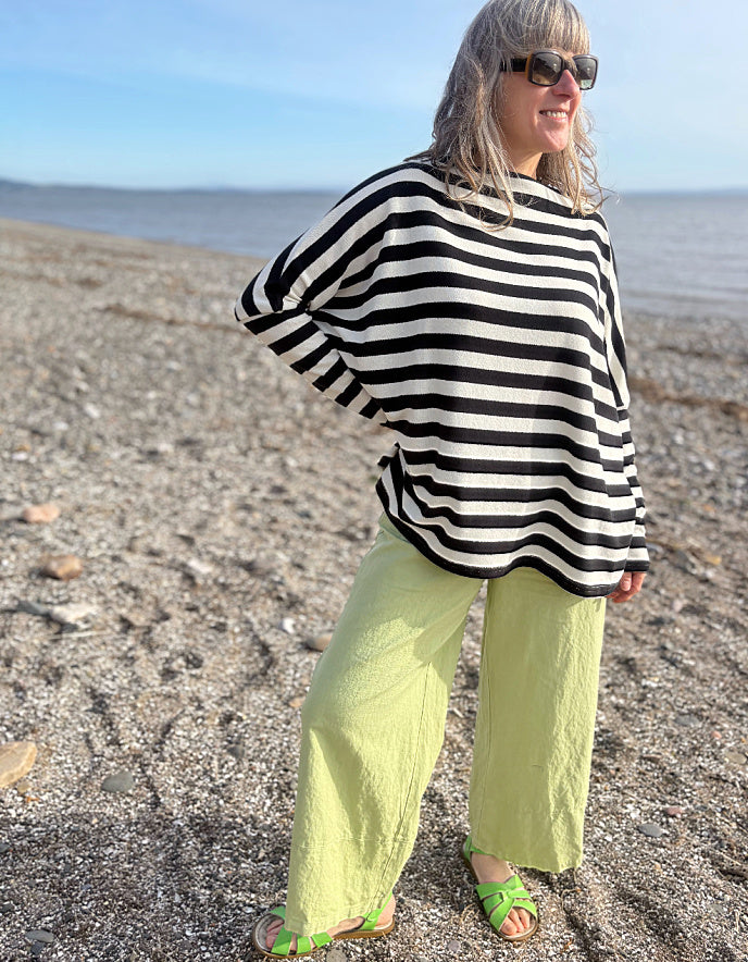 Woman wearing a black and white striped sweater and bright green pants on a beach.