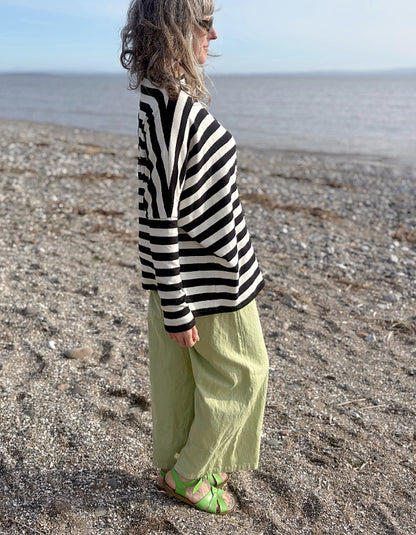 Person wearing a black and white striped sweater on a pebbly beach with ocean view