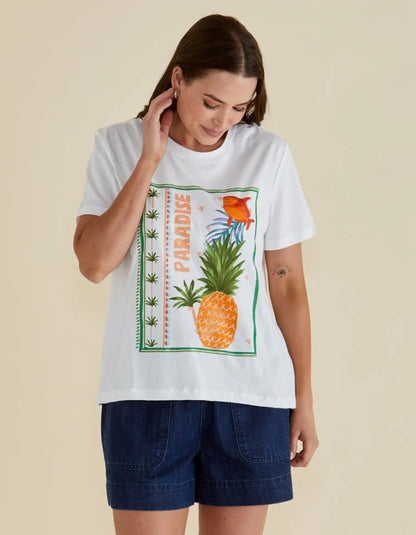 Woman wearing a white t-shirt with a pineapple graphic and 'Paradise' text on a beige background