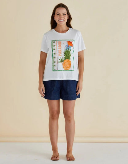 Woman wearing a white t-shirt with a pineapple design and navy shorts against a beige background