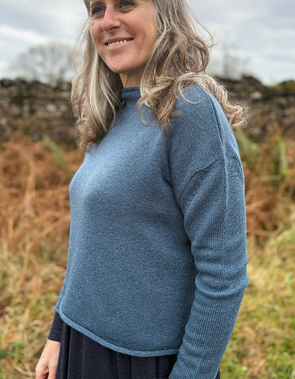 Woman wearing a blue sweater standing outdoors with a natural background