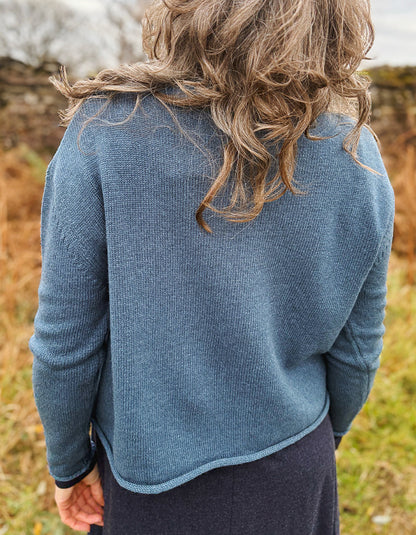 Person wearing a blue sweater standing in a natural setting with blurred background