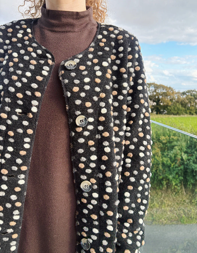 Person wearing a black coat with white and beige polka dot pattern outdoors.