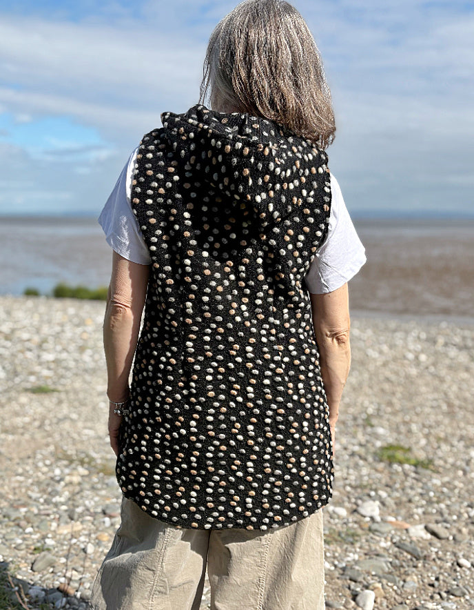 Person wearing a black patterned vest on a beach