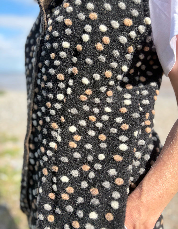 Close-up of a black fabric with white and beige polka dots, held by a person outdoors.