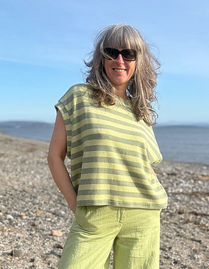 Woman in a striped shirt and pants standing on a beach with ocean in the background