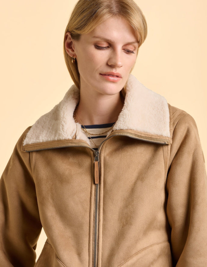 Woman wearing a brown jacket with a white fur collar on a beige background
