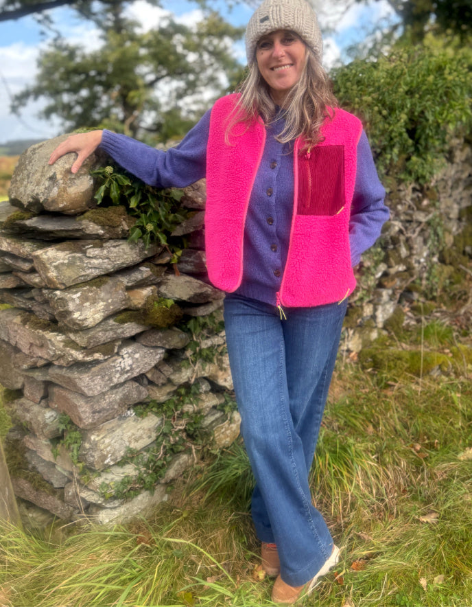 Person wearing a bright pink vest standing next to a stone wall in a natural setting
