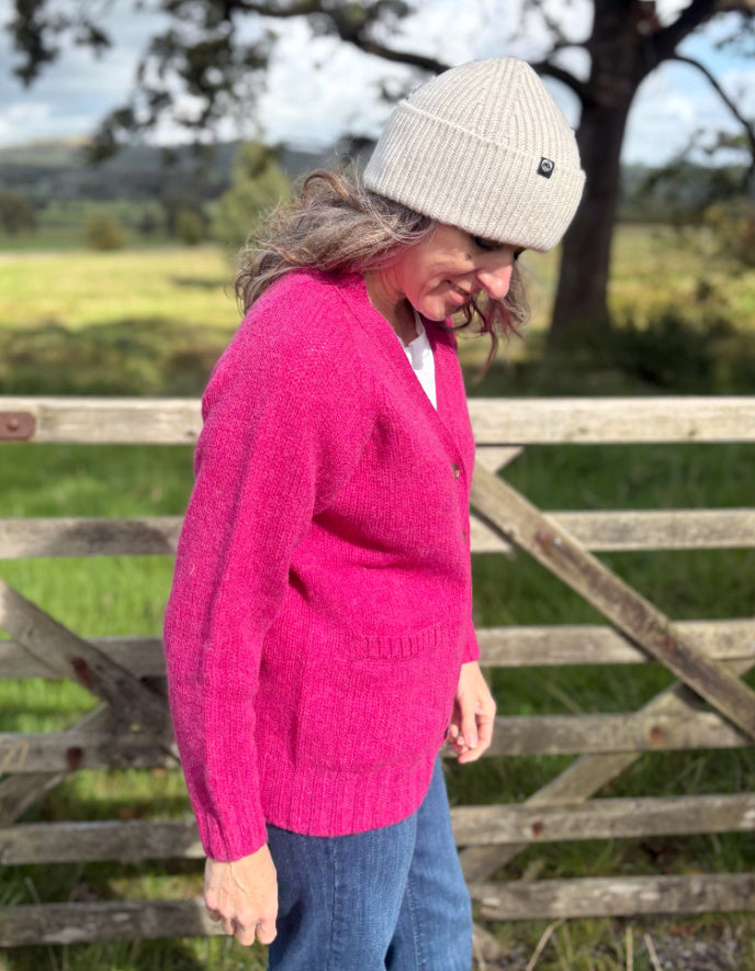 Person wearing a pink sweater and beige beanie standing in a field with a wooden gate.