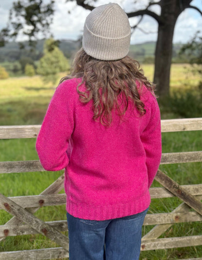 Person wearing a pink sweater and gray beanie standing in front of a wooden fence with a scenic background.