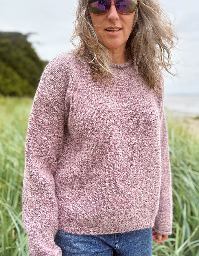 Person wearing a pink sweater and sunglasses in a grassy outdoor setting