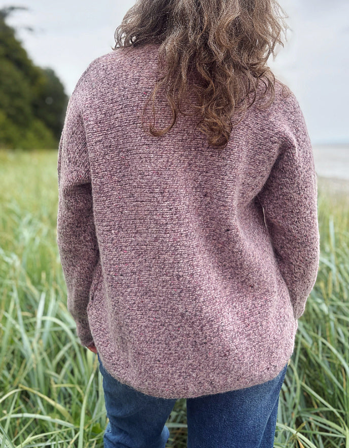 Person wearing a donegal tweed pink sweater and sunglasses in a grassy outdoor setting