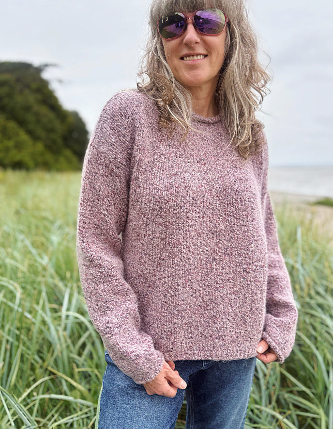 Woman wearing a pink sweater and sunglasses standing in a field.