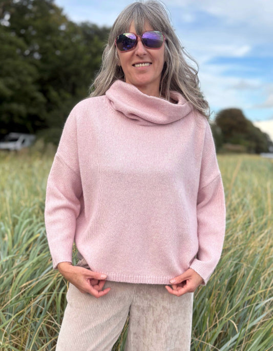 Woman wearing a pink sweater and sunglasses in a grassy field