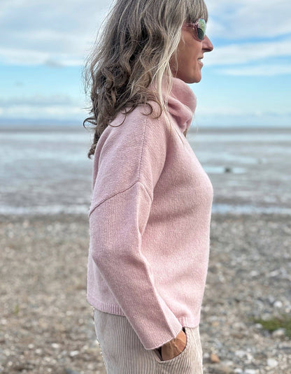Woman wearing a pink sweater on a beach with a blue sky and ocean in the background