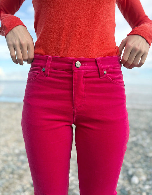 Person wearing a red sweater and pink velvet jeans standing on a beach.