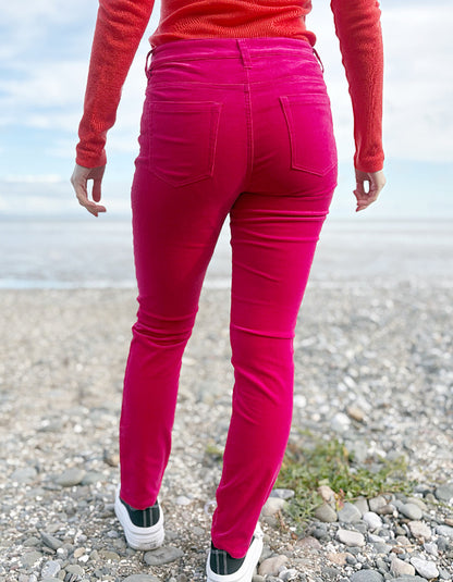 Person wearing a red sweater and pink velvet jeans standing on a beach.