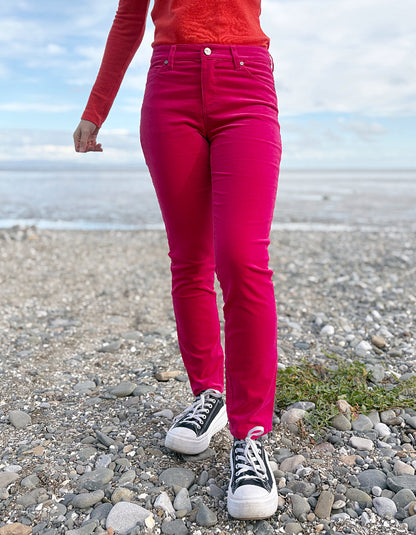 Person wearing a red sweater and pink velvet jeans standing on a beach.