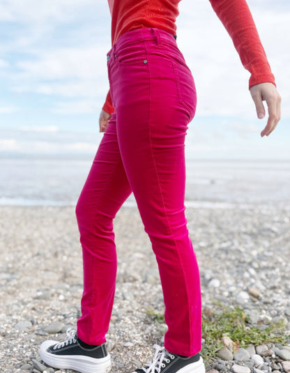Person wearing a red sweater and pink velvet jeans standing on a beach.