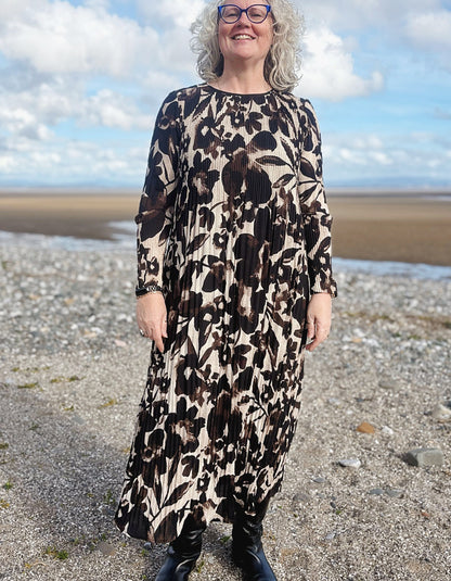 Woman wearing a patterned dress standing on a beach with a blue sky and clouds in the background.