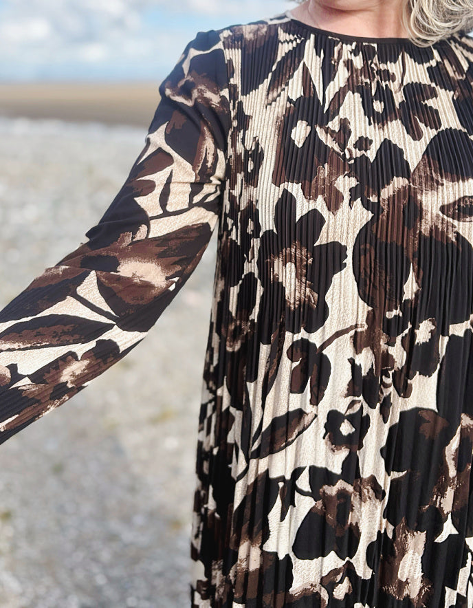 Close-up of a person wearing a pleated dress with a brown and black pattern.