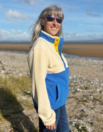 Person wearing a blue and beige jacket on a rocky beach with a blue sky.