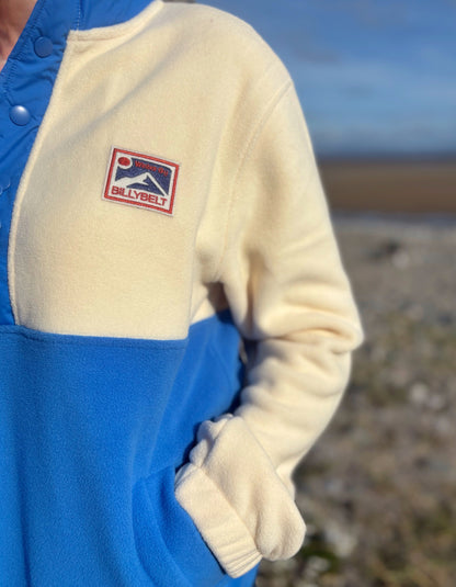 Close-up of a blue and beige outfit with a visible brand logo on a blurred beach background