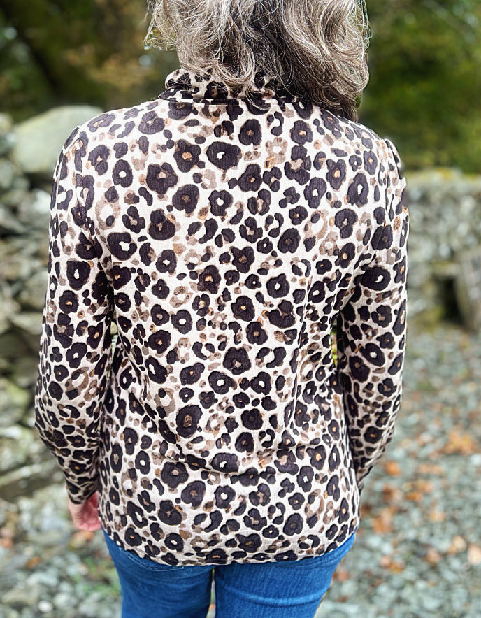 Person wearing a leopard print polo neck top with a blurred natural background