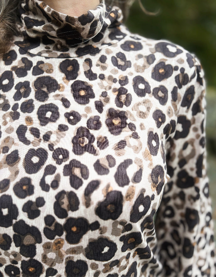 Person wearing a leopard print polo neck top with a blurred natural background