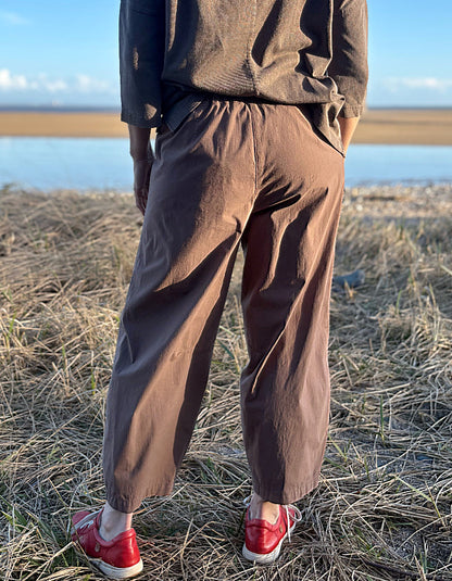 woman wearing brown pants and red shoes standing in a field with a body of water in the background