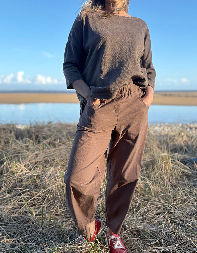 Person wearing a brown cotton and hemp top and brown pants standing on a grassy field with a blue sky in the background