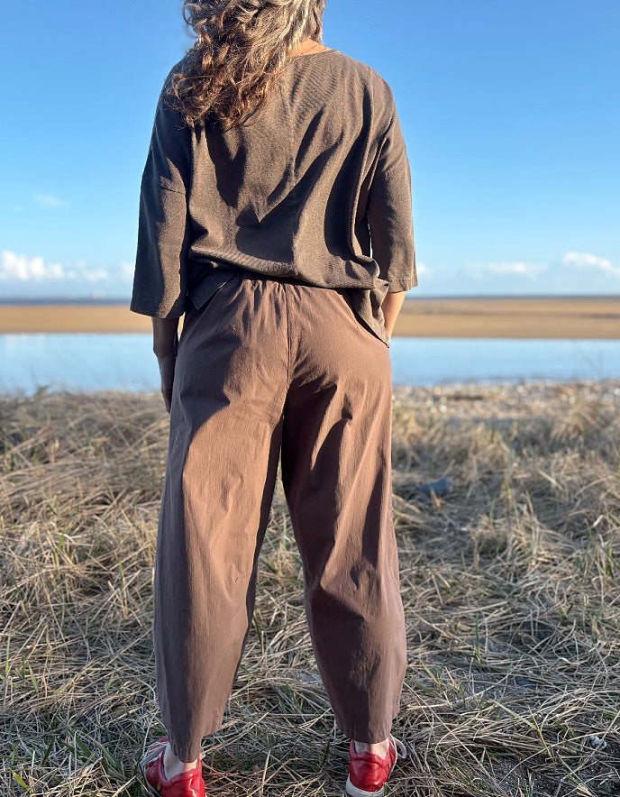 Person wearing a brown cotton and hemp top and brown pants standing on a grassy field with a blue sky in the background