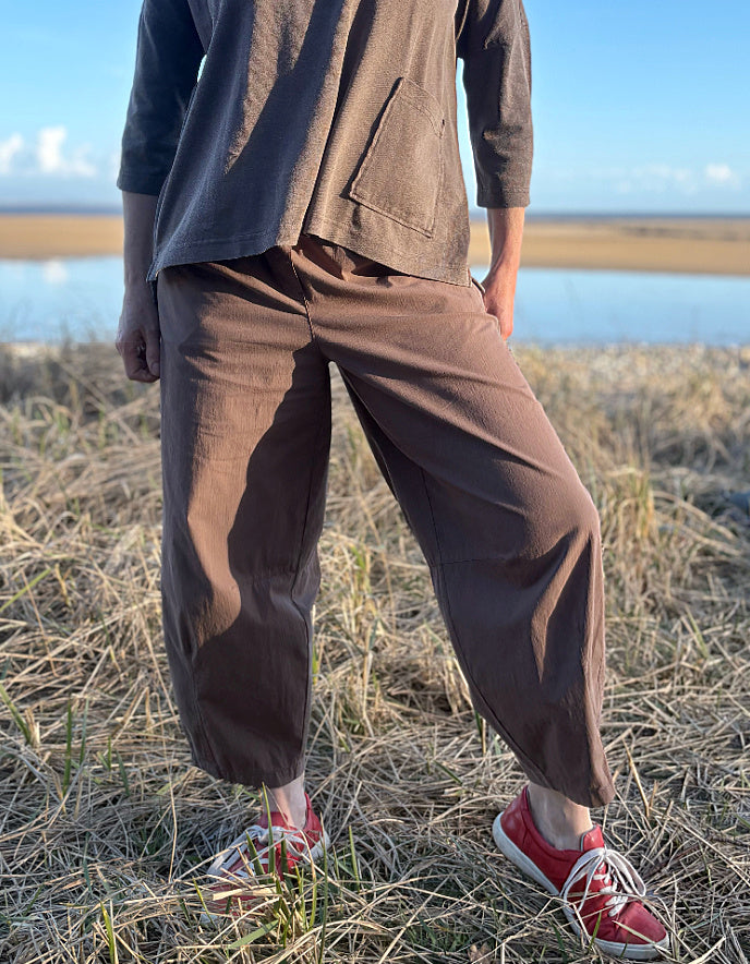 woman wearing brown pants and red shoes standing in a field with a body of water in the background