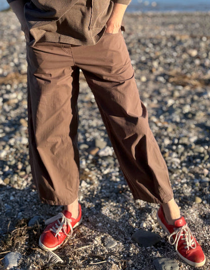 woman wearing brown pants and red shoes standing in a field with a body of water in the background
