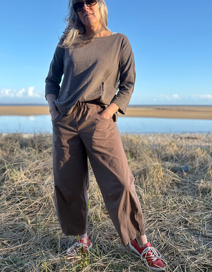 woman wearing brown pants and red shoes standing in a field with a body of water in the background