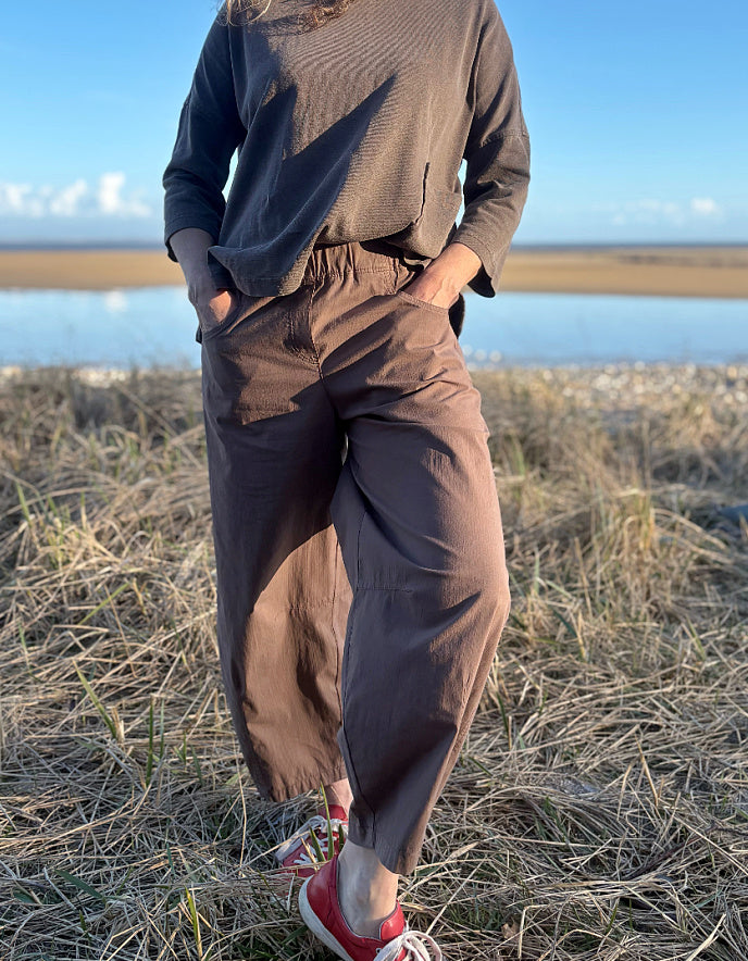 woman wearing brown pants and red shoes standing in a field with a body of water in the background