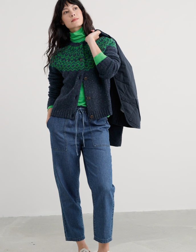 Woman wearing a green sweater, blue jeans, and a dark jacket on a white background