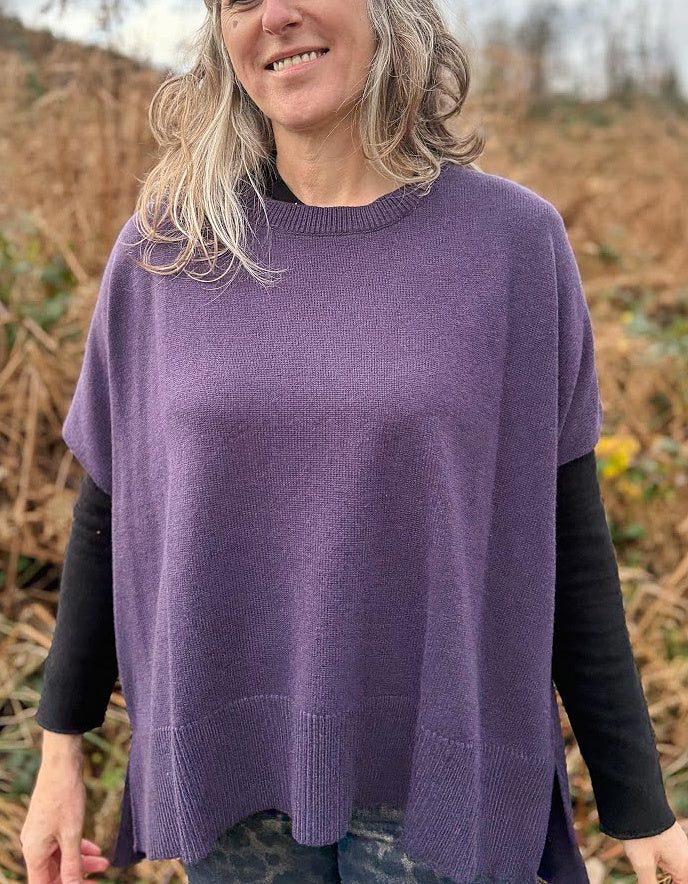 Woman wearing a purple poncho over a black shirt with a natural background