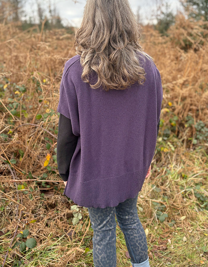 Person wearing a purple sweater standing in a field with dry grass and trees in the background