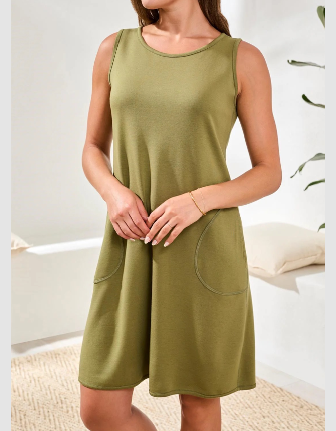 Woman wearing a green sleeveless dress with pockets in a minimal indoor setting.