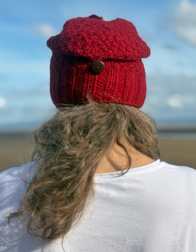 Person wearing a red knitted hat with a button on a beach